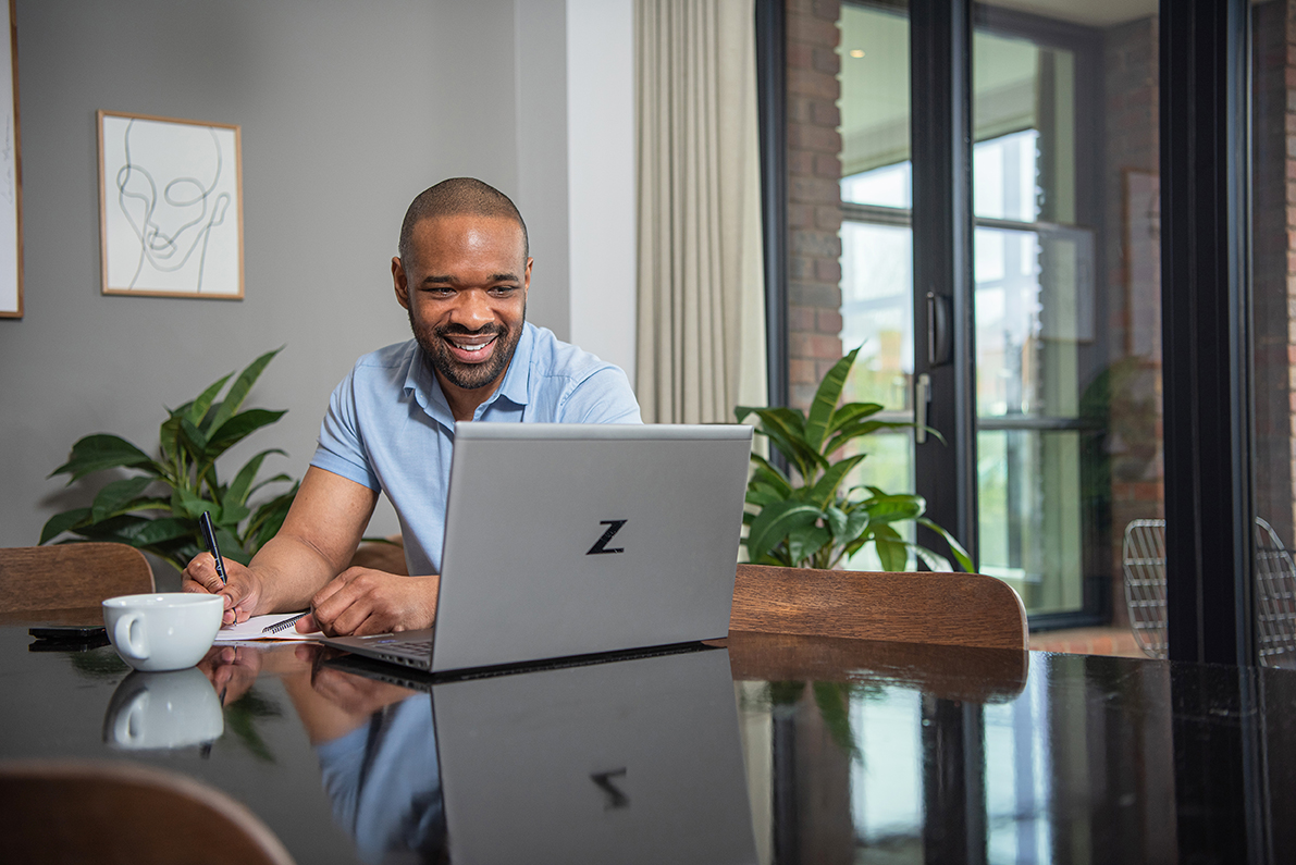 Business traveller smiling while working remotely on a laptop at a dining table in a modern serviced apartment