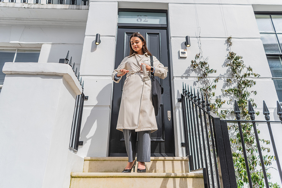 Stylish professional stepping out of a London townhouse, using a smartphone on the go