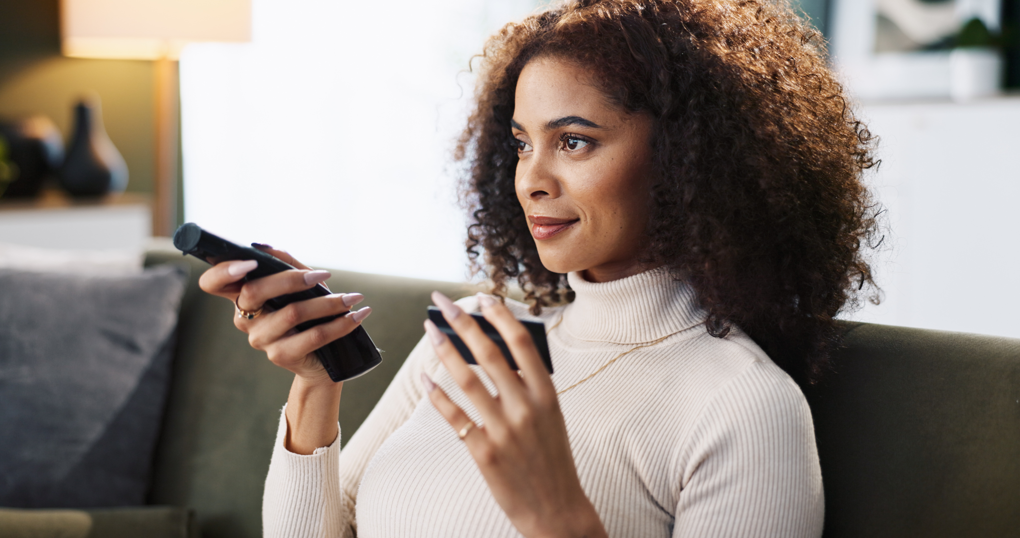 Woman relaxing on a sofa with a drink and remote control in hand.