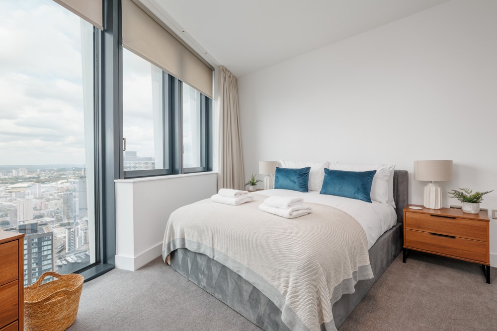 An apartment with a ceiling to floor window with a city view, natural lighting and modern furnishing.