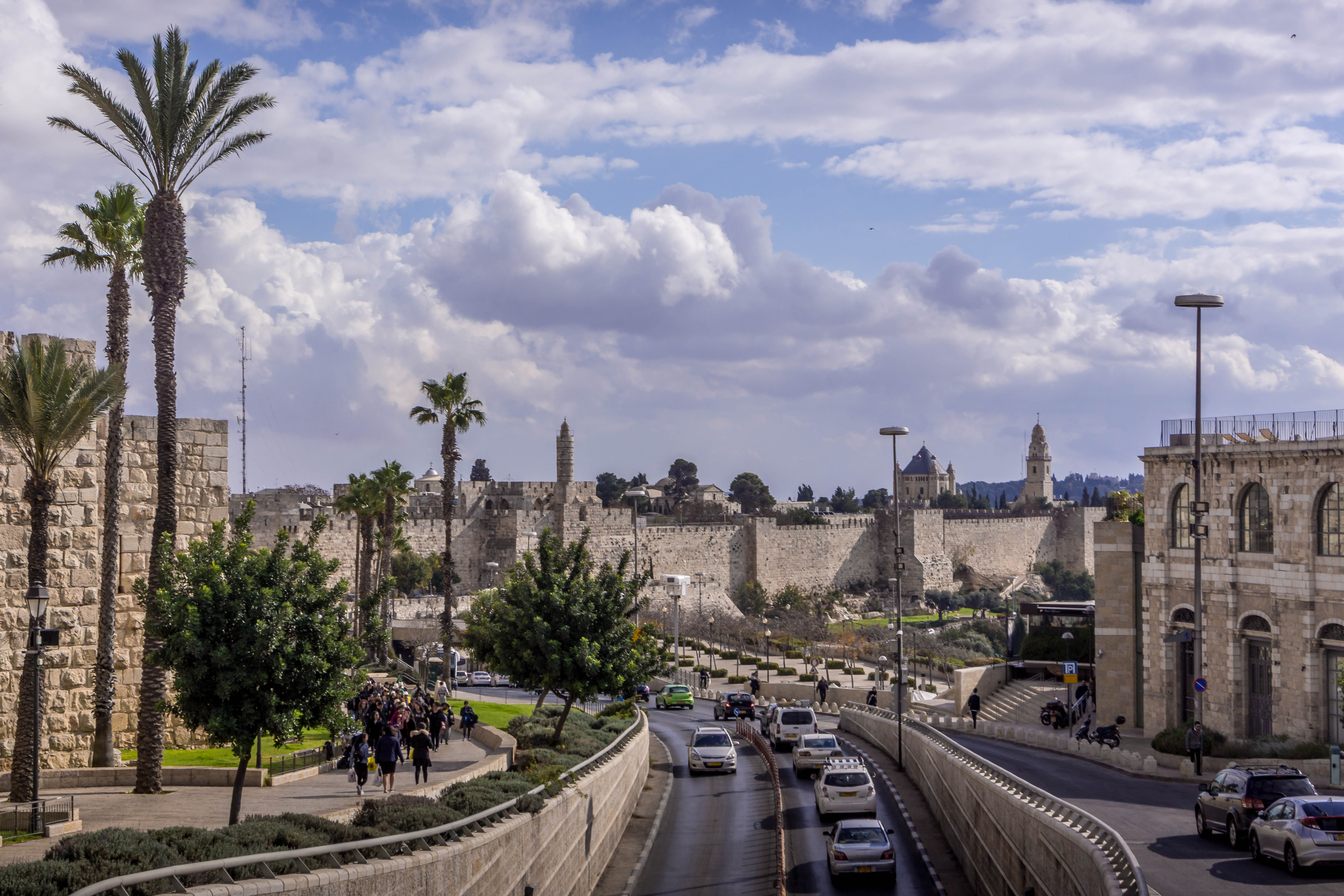 The road traffic on Jerusalem highway going along the walls of the Old town, with the palm trees, and cloudy sky, in Israel.