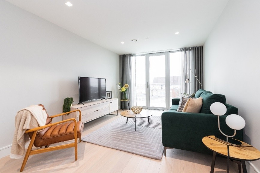 A modern living room with a green sofa, armchair, TV, coffee table, and large glass doors leading to a balcony.