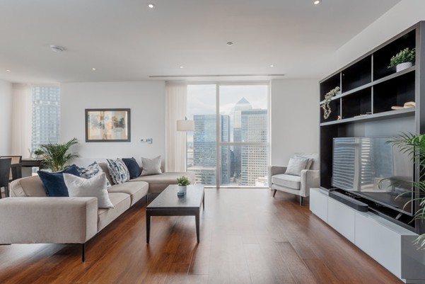 A modern room with a view of the city skyline. Wooden flooring and a light colour palette.
