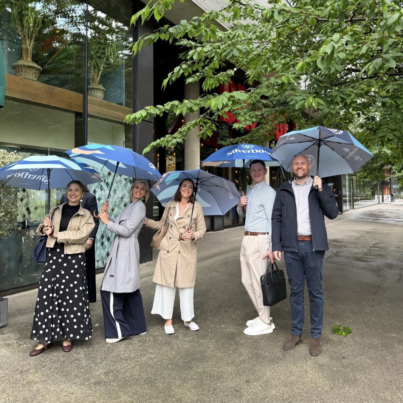 A group of SilverDoor team members stand outdoors holding branded umbrellas on a rainy day outside