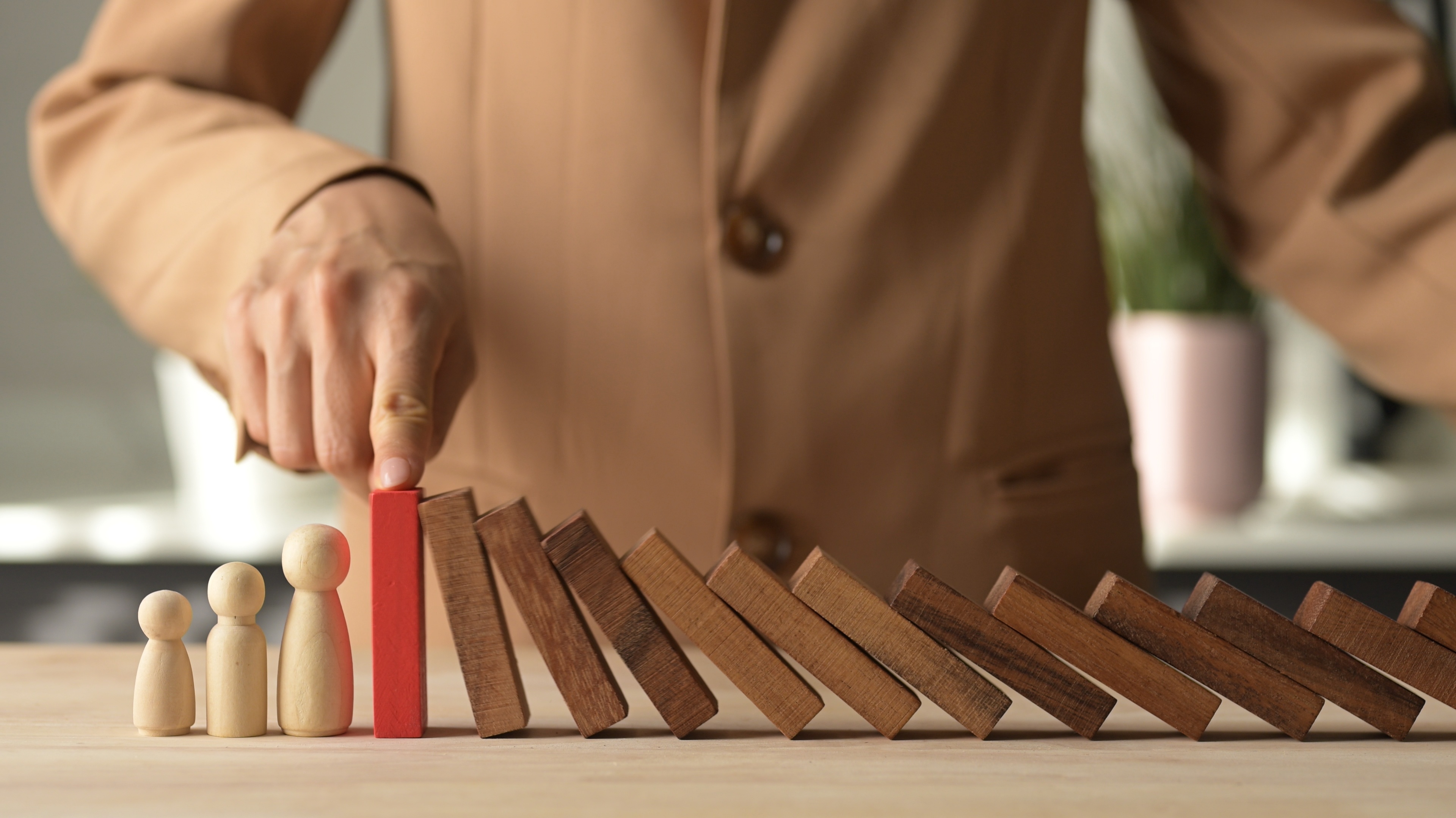 A hand stopping dominoes from hitting a wooden family